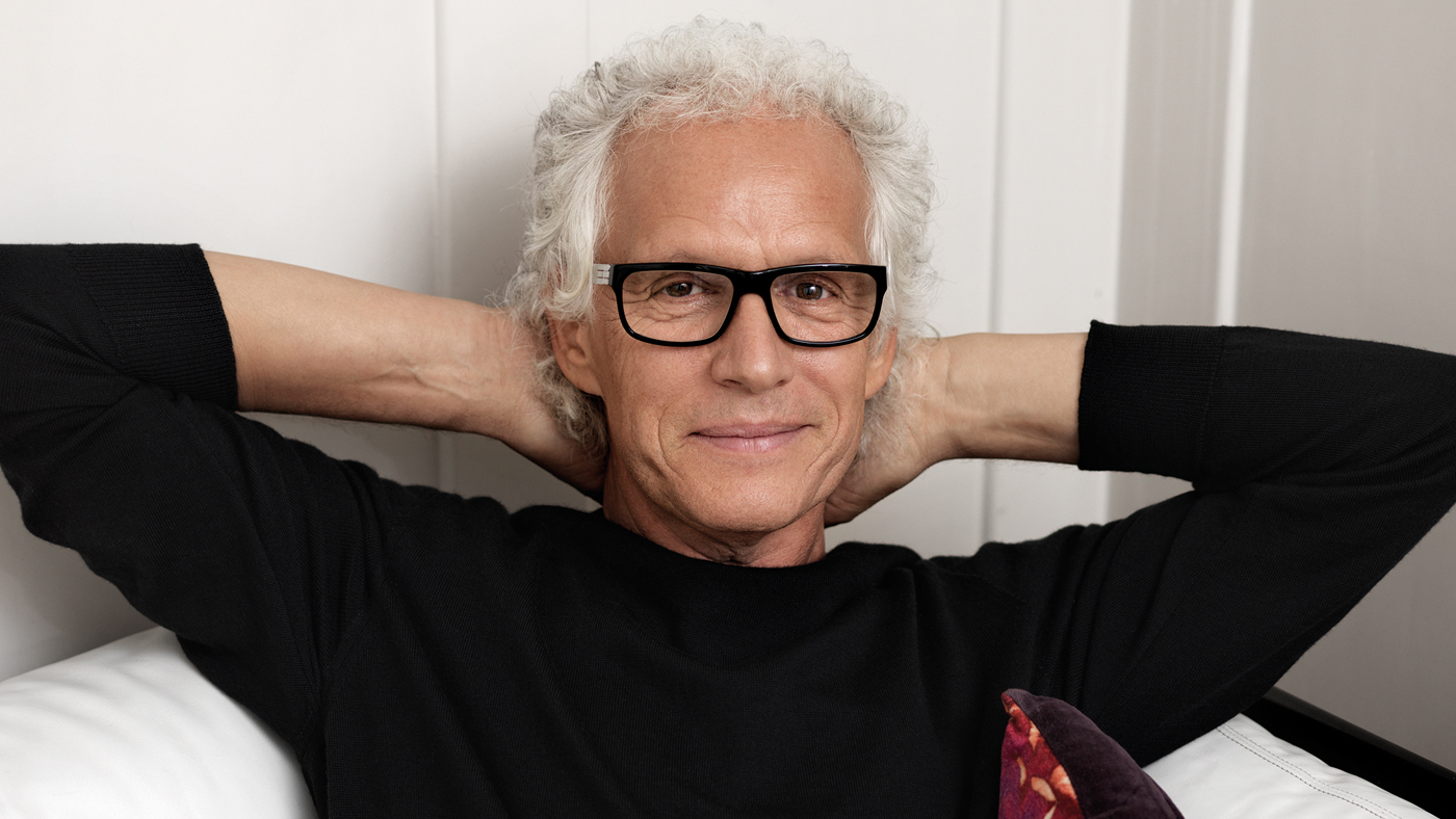 Ein Mann sitzt mit Brille auf einem Sofa und lächelt